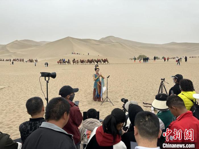 圖為2023年4月底，敦煌大漠“逐舞者”奧楠在鳴沙山月牙泉景區(qū)視頻直播，吸引游人圍觀?！●T志軍 攝